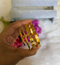 Hand holding Anti-Tarnish 18K gold plated bangle bracelet stack set of 3 — gold nail bangle, rhinestone daisy floral bangle, and celestial star engraved bangle by Aferando