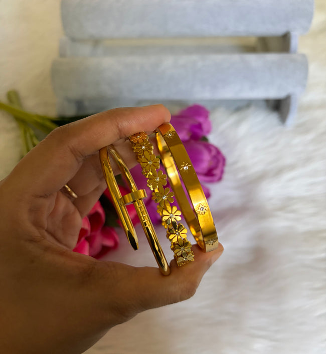 Hand holding Anti-Tarnish 18K gold plated bangle bracelet stack set of 3 — gold nail bangle, rhinestone daisy floral bangle, and celestial star engraved bangle by Aferando