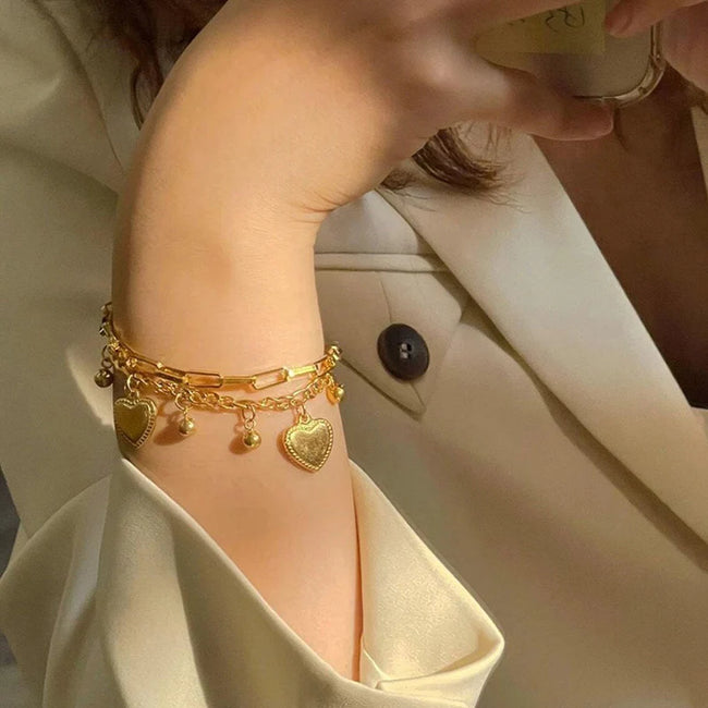 Anti-tarnish 18K gold plated dainty heart charm bracelet 
worn on wrist — stackable gold charm bracelet with 
dangling hearts for women